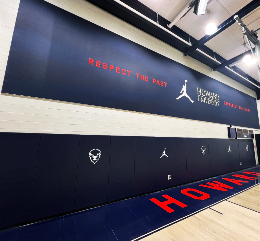 A long, navy blue sign that says "RESPECT THE PAST" along with the university's name and logo of a bison in Howard University's Burr Gymnasium